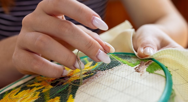 Mâini care brodează cu ac și ață colorată